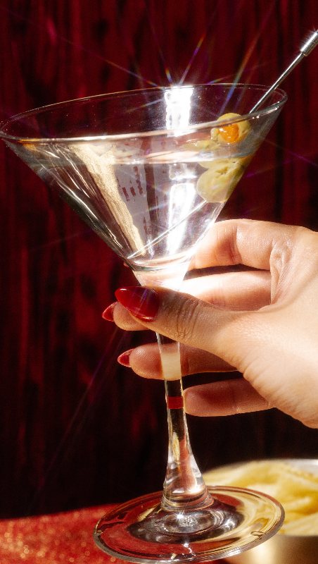 A hand raising a martini with olives in front of red velvet